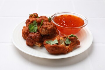 Baked cauliflower buffalo wings with parsley and sauce on white tiled table, closeup