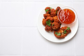 Baked cauliflower buffalo wings with parsley and sauce on white tiled table, top view. Space for text