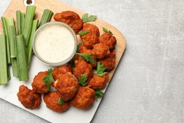 Baked cauliflower buffalo wings with celery and sauce on grey textured table, top view. Space for text