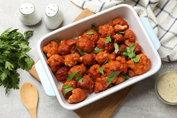 Baked cauliflower buffalo wings with parsley served on grey textured table, flat lay