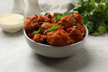 Baked cauliflower buffalo wings with parsley served on grey textured table, closeup