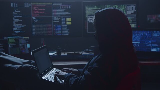 A mysterious hooded figure intently types on a sleek laptop, surrounded by multiple screens displaying intricate code