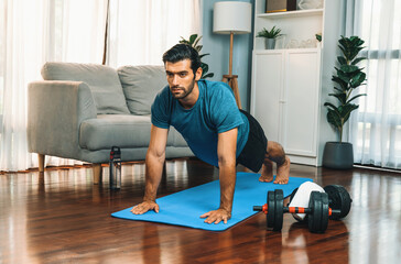 Fototapeta premium Flexible and dexterity man in sportswear doing yoga position in meditation posture on exercising mat at home. Healthy gaiety home yoga lifestyle with peaceful mind and serenity.