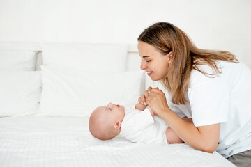 mom and baby, a young beautiful mom with a little boy hugging and playing at home in the bedroom,...