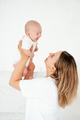 a young beautiful mother with a baby boy hugging on the bed at home in the bedroom, mother's care and love, portrait of a happy mother with a child, healthy motherhood