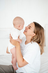 a young beautiful mother with a baby boy hugging on the bed at home in the bedroom, mother's care and love, portrait of a happy mother with a child, healthy motherhood