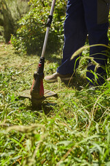 Obraz premium Gardener with a grass trimmer cutting overgrown grass and weeds around the building.