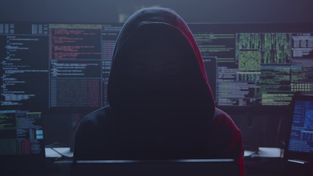 In a dimly lit, shadowy room, a cloaked figure stands amidst numerous glowing screens, showcasing intricate code