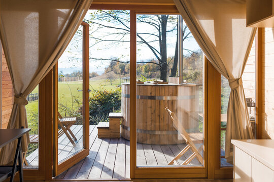 Empty glamping cabin with large panoramic windows and a private wooden hot tub on a terrace. Weekend getaway concept.