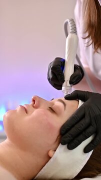 Close-up of a cosmetologist manipulating a hydropeeling device to cleanse and rejuvenate facial skin. A woman undergoes a facial treatment in a professional beauty salon.