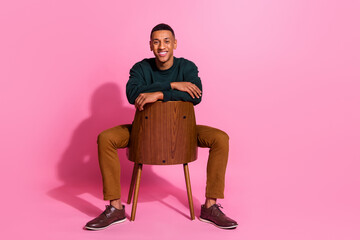 Full length photo of attractive funny guy wear sweatshirt sitting armchair smiling emtpy space isolated pink color background