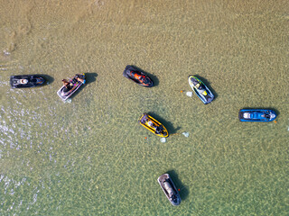 Aerial photo of jet skis anchored in clear, shallow water with people wading nearby. The vibrant...