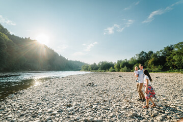 Mother, father hug baby son walking on beach near lake. Father's, mother's, Children's day. Spending time together. Mom, dad embrace child at sunset. Happy family holiday in summer.