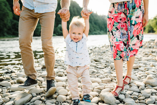 Bottom view of legs. Mother, father holding hands baby son walking on stone beach closeup. Hold hands. Happy family holiday in summer. Spending time together. Mom, dad, child at sunset. View down.
