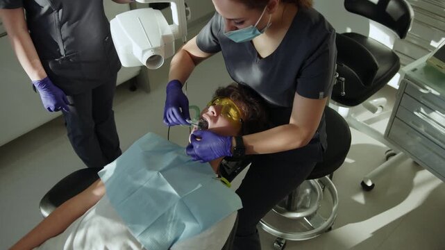 Shot from top assistants and man dentist in medical masks hold dental instrument that treats teeth. Hydience and healthy