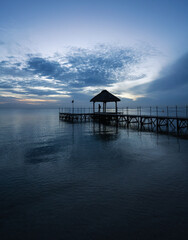 A woman stands on a pier enjoying the silence during the blue hour at Flic en Flac beach, Mauritius, Africa.