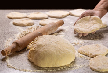 Process of making pies. Baking at home. Homemade cakes dough in the women's hands. Woman rolling out dough on kitchen table, close up. Hands baking dough with rolling pin on wooden table