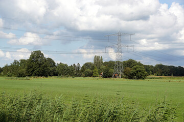 Dutch countryside with Electricity Pylon in a field. Meadows, grass, trees, farm. Blue sky with...