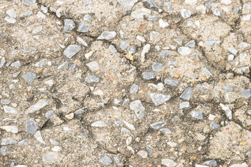 A cracked sidewalk with a lot of rocks on it. The sidewalk is old and worn down. The rocks are scattered all over the ground, making it look like a rocky terrain. Scene is one of decay and neglect
