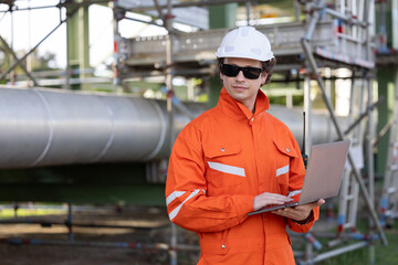 Engineer with laptop working at the pipeline of the oil refinery