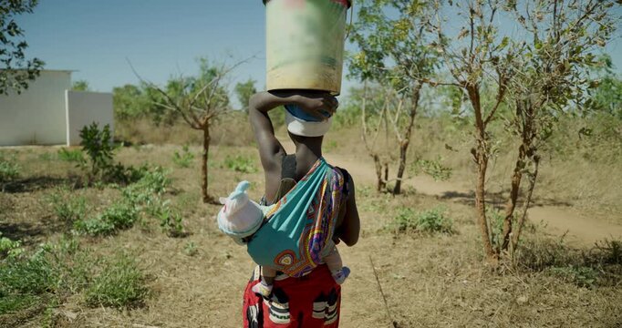 Beautiful slow motion shot following African woman carrying baby and bucket 
