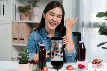 Smiling young beautiful Asian reviewing tasty mixed strawberry and cherry juice detox drinks, showing healthy product to promote for special promotion selling on social media online record. Stratagem.