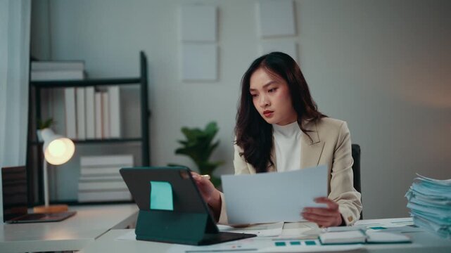 Business woman analyzing documents, looking stressed, and rubbing eyes while working at the office. Piles of paperwork and a laptop on the desk