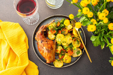 A hearty delicious dinner, baked rabbit with potatoes and carrots, a set table with food, a glass of wine and a vase of flowers