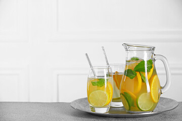 Freshly made lemonade with mint in jug and glasses on light grey table, space for text