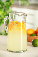 Refreshing lemonade with orange and lime in jug on white wooden table, closeup