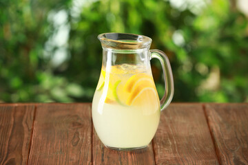 Refreshing lemonade with orange and lime in jug on wooden table against blurred green background