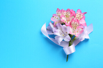 Beautiful alstroemeria flowers and ribbon on light blue background, top view. Space for text