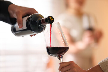Man pouring red wine into woman`s glass indoors, selective focus