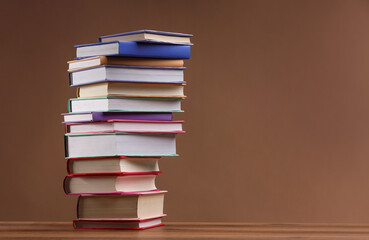 Stack of colorful books on wooden table against light brown background, space for text