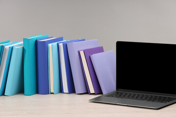 Colorful books and laptop on white wooden table against light grey background