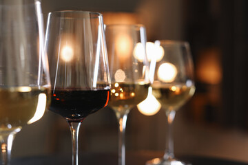 Different tasty wines in glasses against blurred lights, closeup