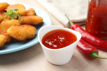 Spicy chili sauce in bowl and chicken nuggets on wooden table