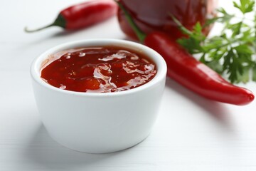Spicy chili sauce in bowl on white wooden table, closeup