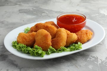 Tasty chicken nuggets with chili sauce and lettuce on grey textured table