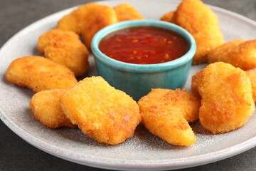 Plate with hot chili sauce and nuggets on grey table, closeup