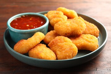 Plate with hot chili sauce and nuggets on wooden table, closeup