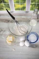 Vertical photo of dairy products butter eggs milk and bowl of white flour on kitchen counter by window