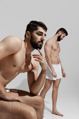 Two men in white shorts sit closely together, their expressions focused and contemplative against...