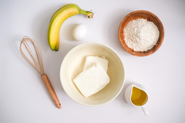 Baking ingredients: flour, egg, whisk, oil and cottage cheese, banana on a white concrete background. Copy space, top view. Baking concept.