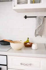 Baking ingredients: flour, egg, whisk, oil, bowl with cottage cheese on a white kitchen table, pan on the oven. Copy space, top view. Baking concept.