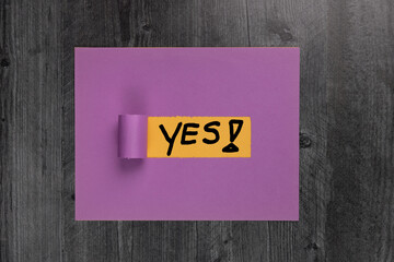 The world Yes! Handwritten on yellow and purple construction paper flat lay background.