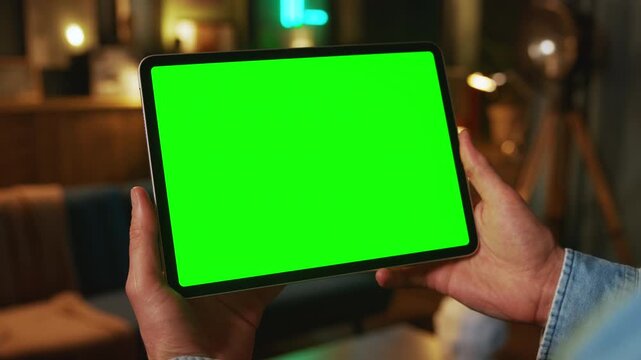 Close up hands holding on tablet computer with horizontal green screen. Mock up. In the evening. Work