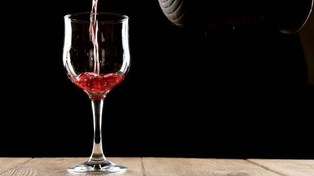 A person pouring red wine from an amphora into a glass . slow motion