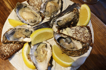 seafood and white wine in a glass. plate with oysters, lemon and bread with butter on a wooden table
