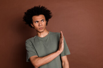 Portrait of young guy dissatisfied guy with curly hair wearing gray t shirt showing stop gesture bad idea isolated on brown color background